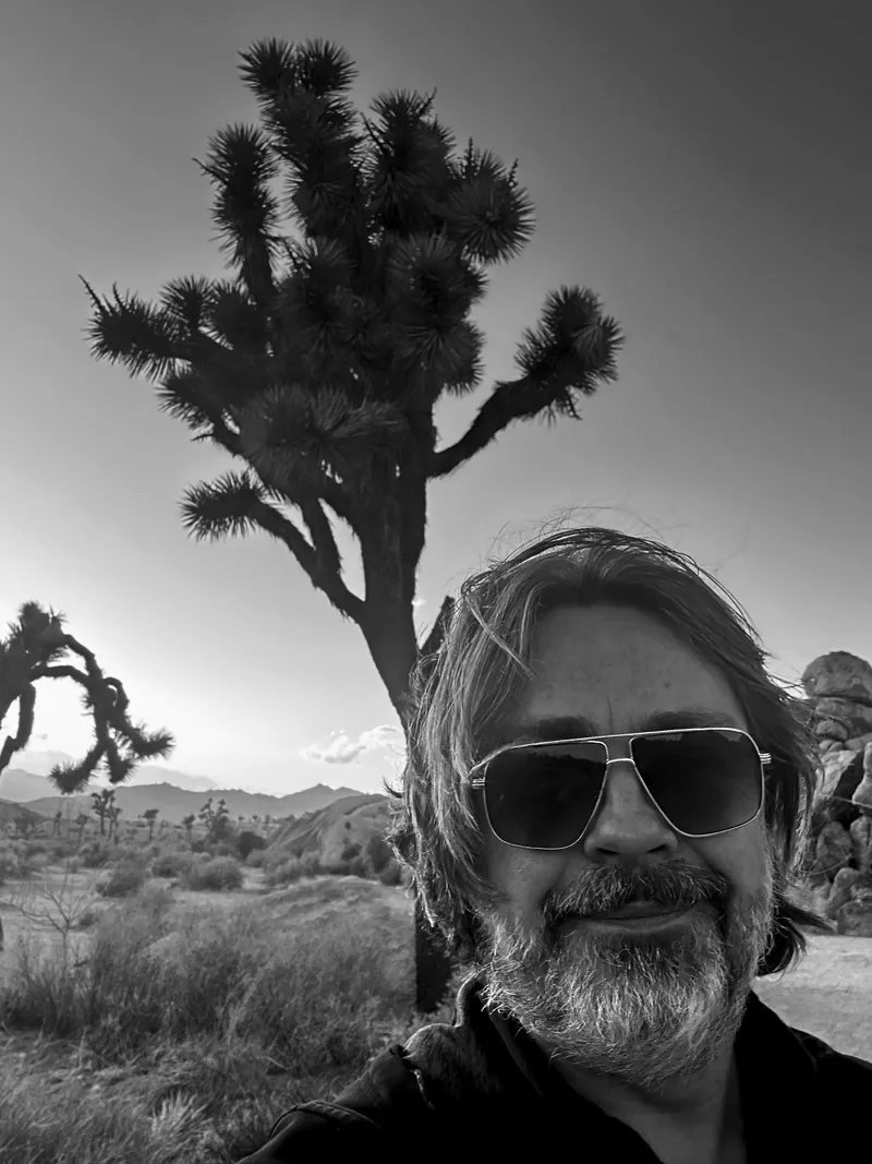 Keith Hanlon in sunglasses in front of a Joshua tree, black and white